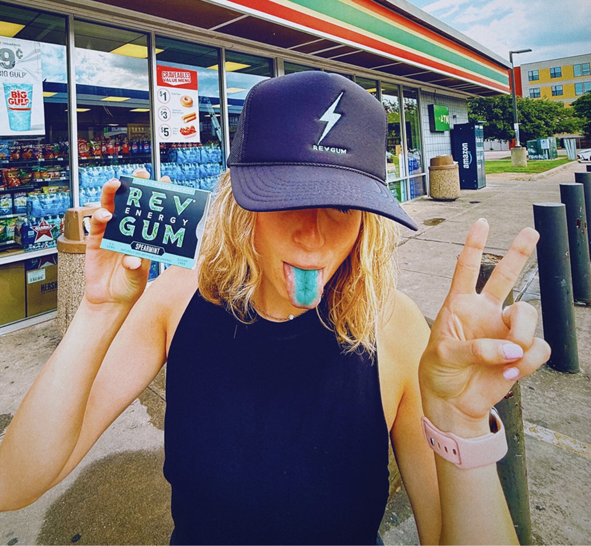 Person wearing a cap and holding REV Energy Gum in front of a convenience store.