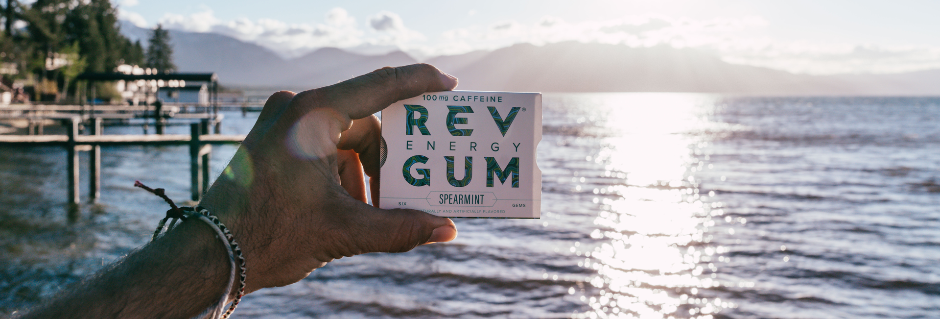 A photo of a hand holding a pack of gum with the ocean as a backdrop.