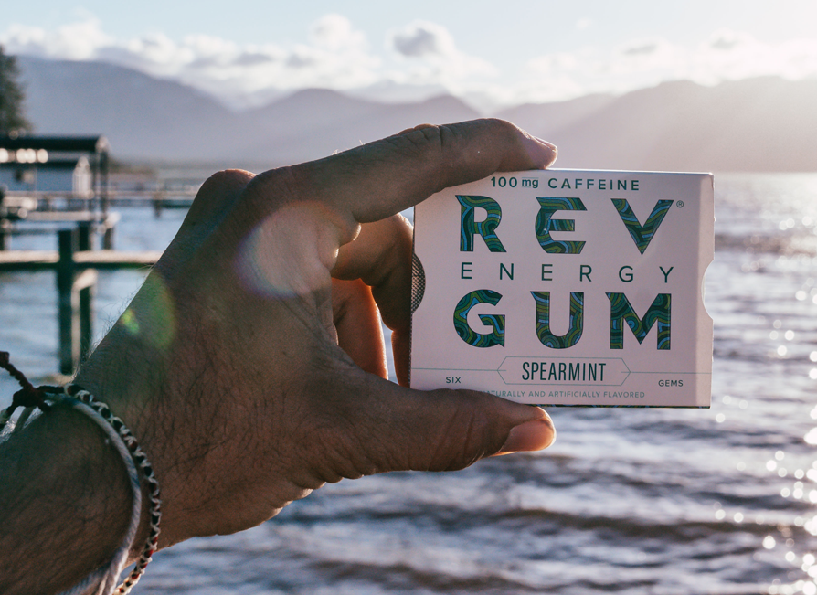 A photo of a hand holding a pack of gum with the ocean as a backdrop.