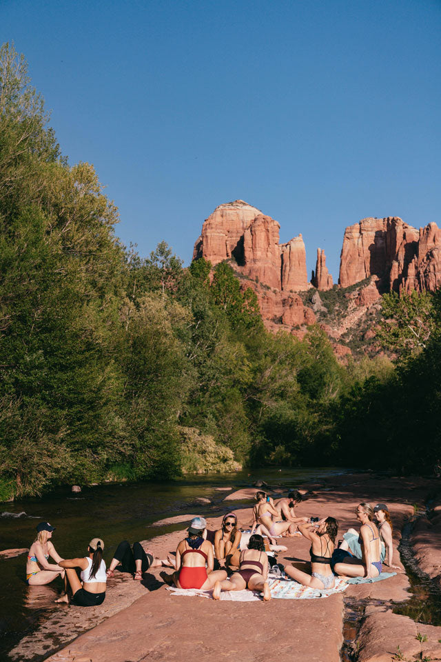 A photo of a group of people in bathing suits laying on the side of a river surrounded by trees.
